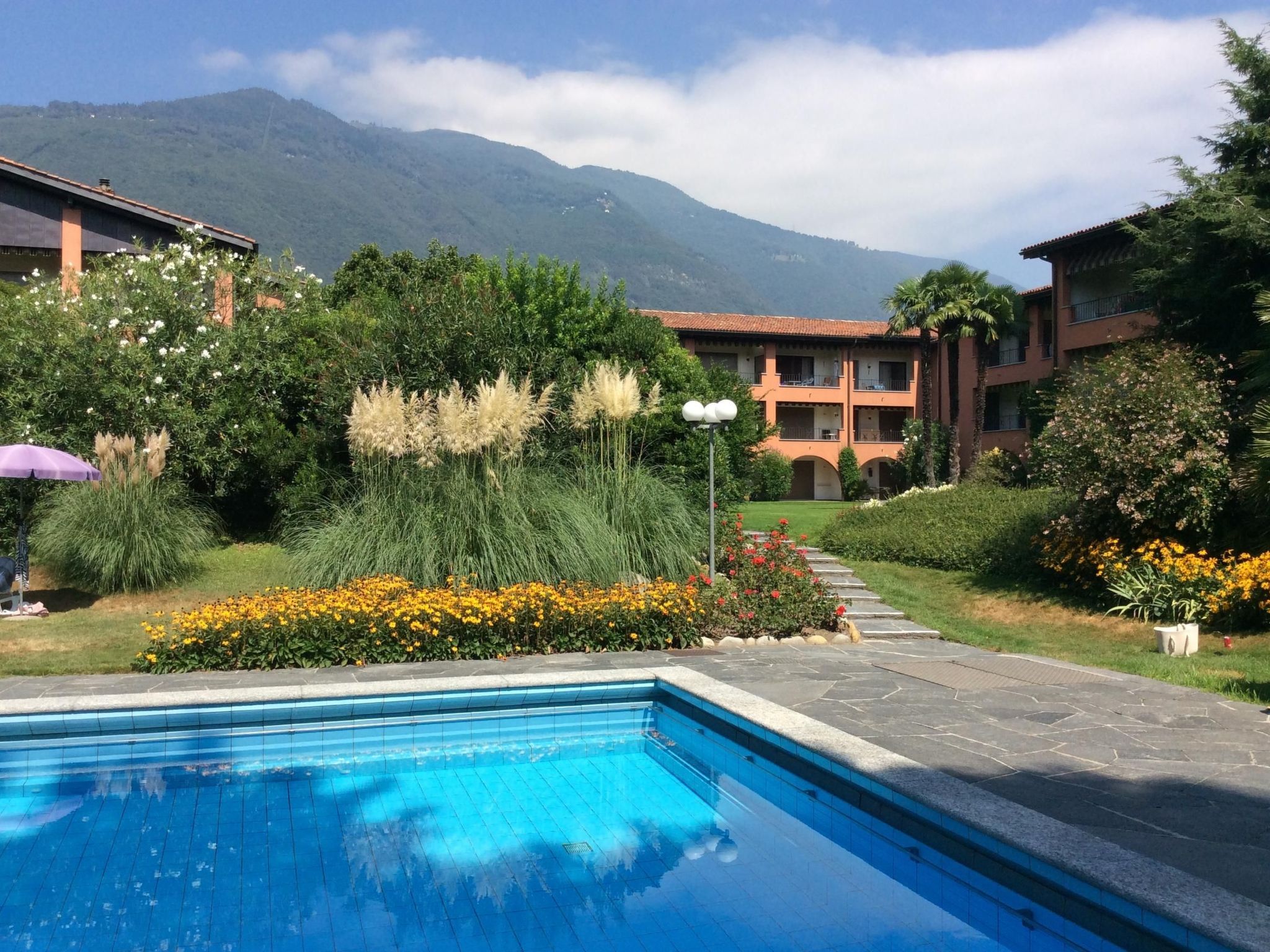 A hotel with a swimming pool, surrounded by lush greenery and a mountain backdrop.