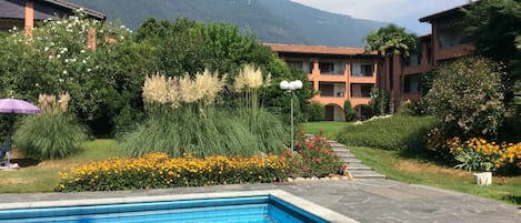 A hotel with a swimming pool, surrounded by lush greenery and a mountain backdrop.