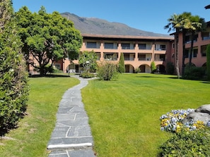 A hotel courtyard with a stone pathway, green lawn, and a building with multiple balconies. - Residenza Sabrina App. 09 by Interhome (Ascona)