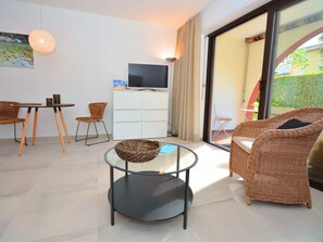 A modern living room with a glass table, wicker furniture, a television, and a sliding glass door leading to an outdoor area. - Residenza Sabrina App. 09 by Interhome (Ascona)