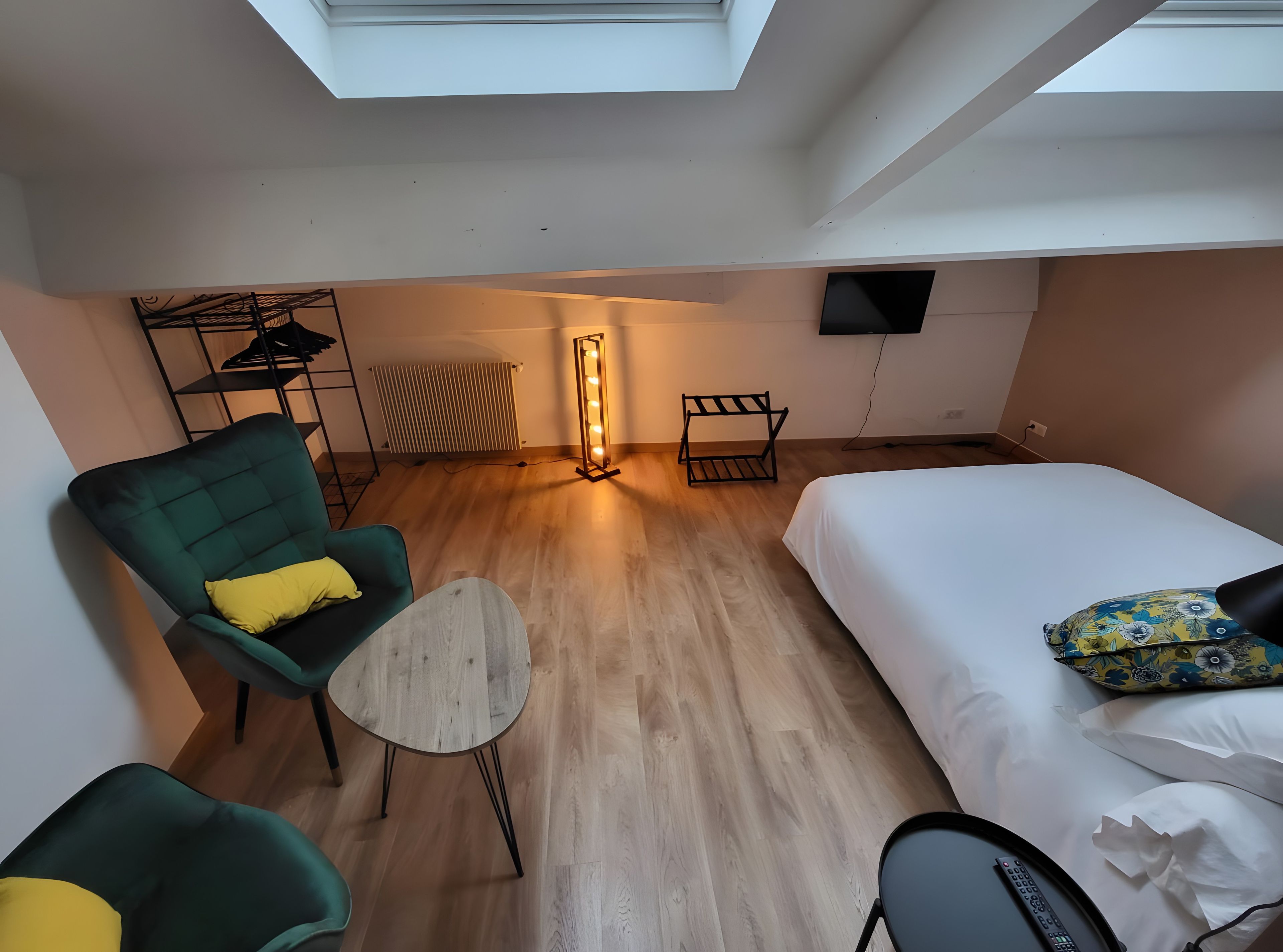 Een moderne hotelkamer met dakraam, een bed, een groene fauteuil, een klein tafeltje en een radiator.