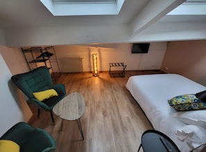 Una camera d'albergo moderna con un lucernario, un letto, una poltrona verde, un tavolino e un termosifone.