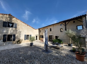 Un cortile con fondo in ghiaia, una scultura al centro e un edificio con diverse finestre e porte.
