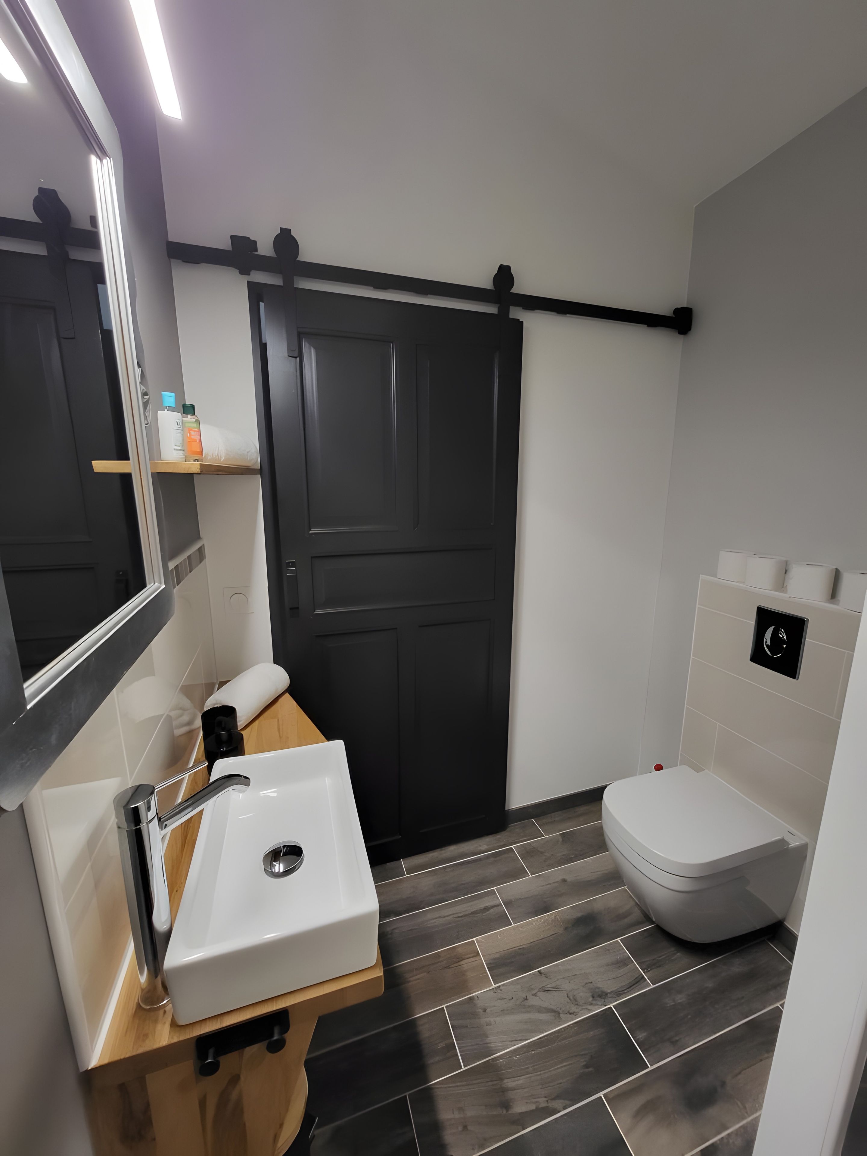 A modern bathroom with a white sink, a toilet, and a black door.
