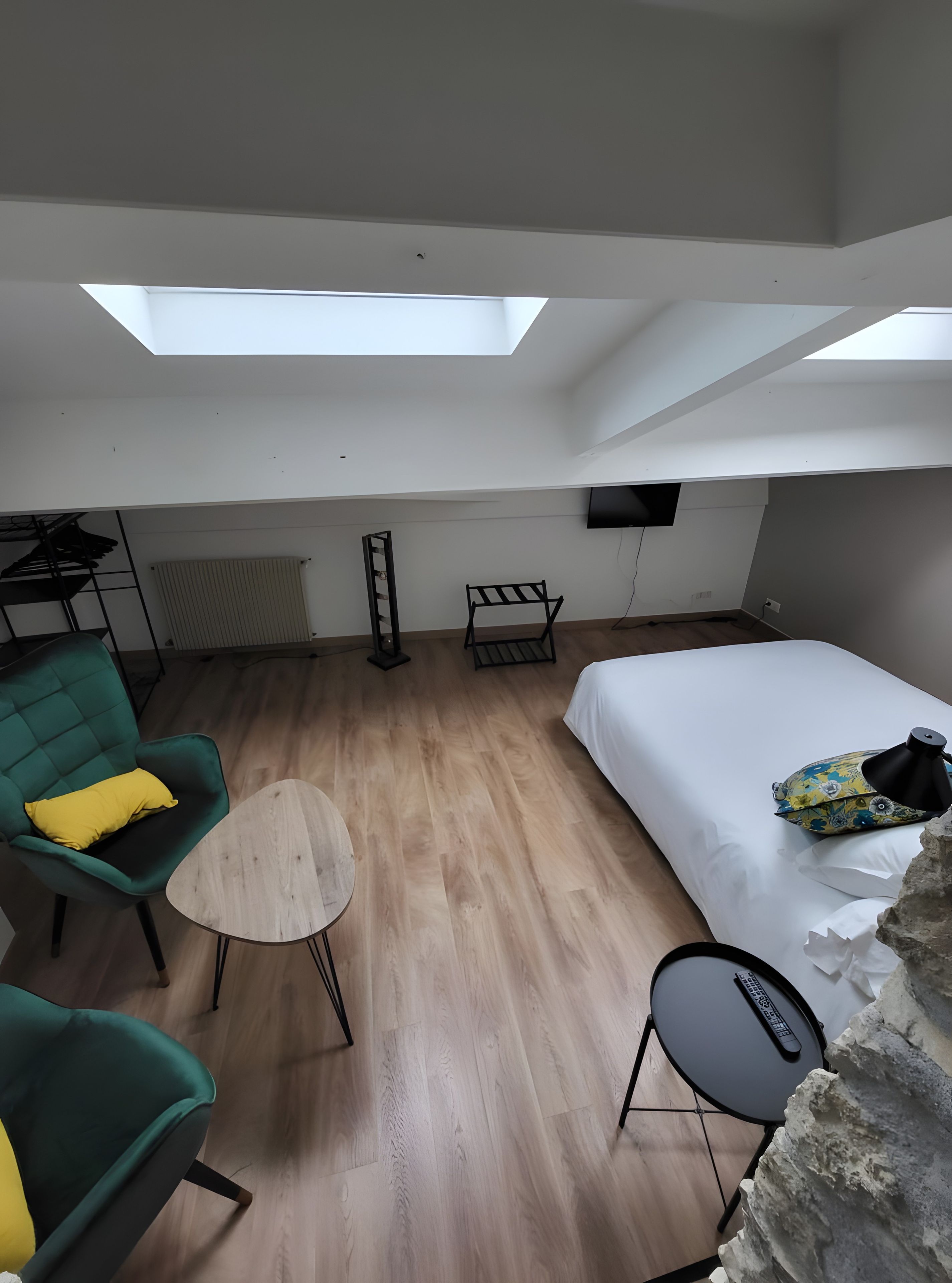Een kamer met een bed, een groene fauteuil, een klein rond tafeltje, een aan de muur bevestigde televisie en een dakraam.
