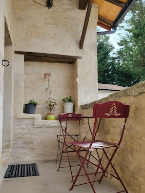 Una zona relax esterna in stile rustico, con un muro in pietra, travi in legno al soffitto e una sedia pieghevole in metallo.