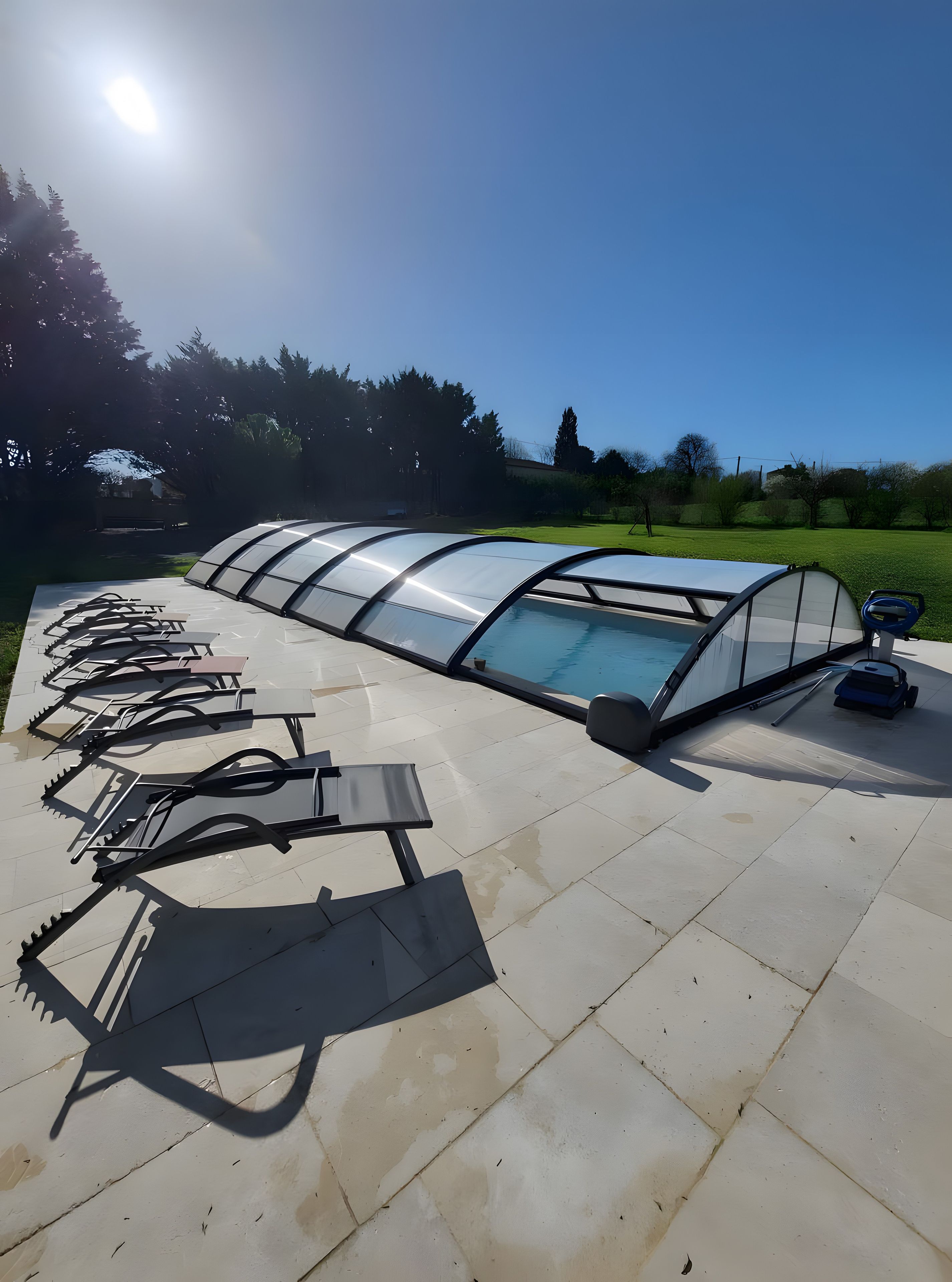Ein Poolbereich mit einer transparenten Dachkonstruktion, umgeben von einer gefliesten Terrasse.