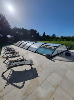 Ein Poolbereich mit einer transparenten Dachkonstruktion, umgeben von einer gefliesten Terrasse.