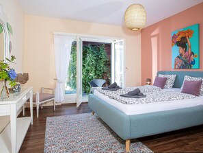 A bedroom with a bed, a chair, a table, a painting, and a view of greenery outside. - Casa Gioia by Interhome (Gerra)