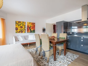 A modern hotel room with a bed, a sofa, a dining table with chairs, a kitchen area, and two paintings on the wall. - Casa Gioia by Interhome (Gerra)
