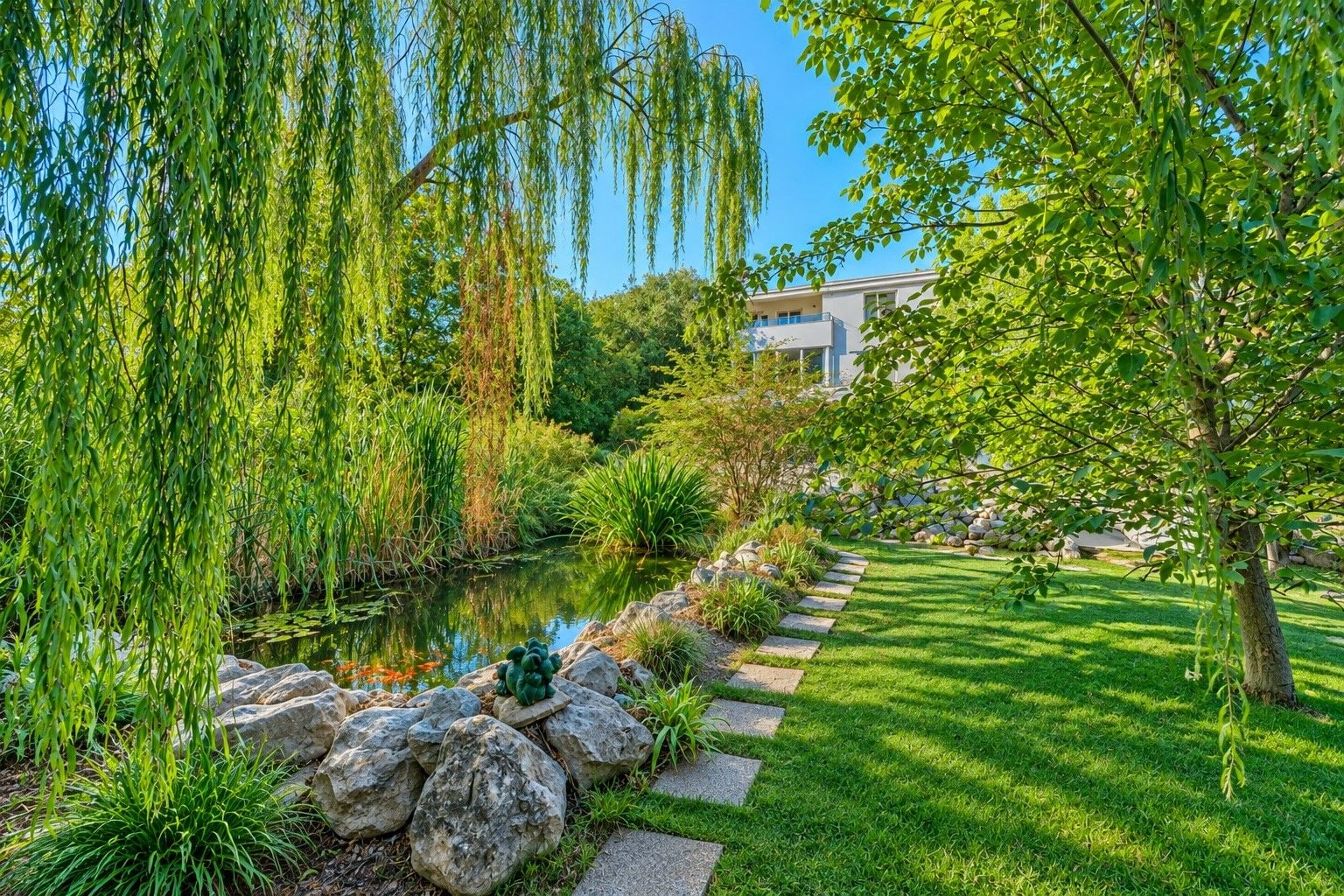 A landscaped garden with a pond, rocks, and a pathway leading to a building.