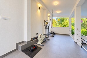 Ein modernes Fitnessstudio mit Trainingsgeräten, einem Hantelständer und Blick auf Grünflächen.