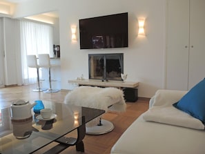 Una sala de estar moderna con una mesa de centro de vidrio, sofá blanco y un televisor de pantalla plana montado sobre un mueble.
