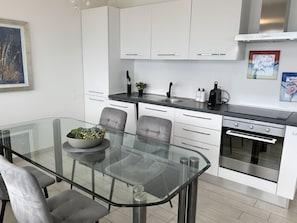 A modern kitchen with white cabinets, a glass dining table, and a built-in oven. - Belinda by Interhome (Minusio)