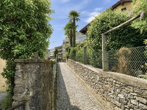 A cobblestone pathway flanked by stone walls and greenery, leading to a building with a sloped roof. - Belinda by Interhome (Minusio)