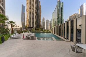 A rooftop pool area with lounge chairs and a small table, surrounded by high-rise buildings. - Luminous 1BR with Stunning Burj Khalifa View (Business Bay, Dubai)