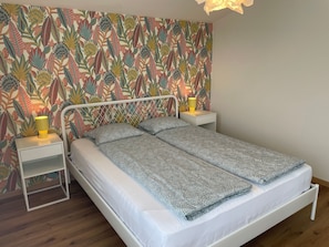 A bed with a patterned bedspread, two bedside tables with lamps, and a floral wallpaper. - Casa Colombina & Studio by Interhome (Gordola)