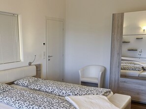 A bedroom with two beds, a chair, a mirror, and a window with blinds. - Casa Makatea by Interhome (Brione sopra Minusio)