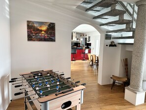 A room with a foosball table, a dining area with chairs, and a kitchen in the background. - Casa Makatea by Interhome (Brione sopra Minusio)