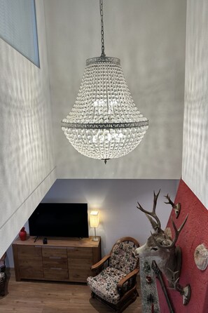A room with a chandelier, a wooden cabinet, a chair, and antler decorations. - Casa Makatea by Interhome (Brione sopra Minusio)