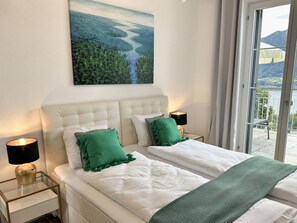 A bedroom with two beds, a painting of a landscape, and a view of a body of water through a window. - Villa Grande Dame by Interhome (Minusio)