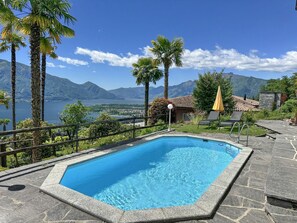 A swimming pool with a stone border, surrounded by palm trees and a mountain view. - Villa Grande Dame by Interhome (Minusio)