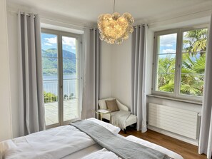 A bedroom with a bed, a chair, a table, and a view of a lake and mountains. - Villa Grande Dame by Interhome (Minusio)