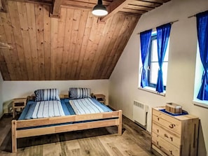A bedroom with a sloped ceiling, a wooden bed, a dresser, and a window with curtains.