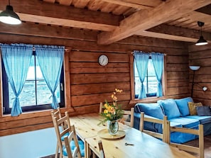 Ein Holzblockhaus-Interieur mit einem Esstisch, Stühlen, einer Couch und einer Uhr an der Wand.