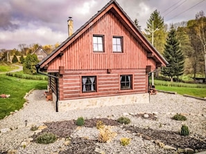 A two-story wooden house with a sloped roof, a chimney, and a gravel driveway.