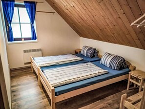 A room with a sloped ceiling, a bed with striped bedding, a small bedside table, and a window with blue curtains.