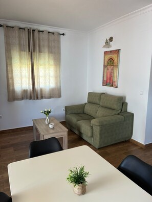 A living room with a green sofa, a small table with a plant, and a wall-mounted lamp. - Casa Luna I        . (El Colorado (Conil de la Frontera))