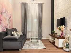 A modern living room with a grey sofa, a glass coffee table, a white cabinet, and a large flat-screen TV mounted on a textured wall. - Apartment for 8 guests in Jewish Disctrict Cracow, Bożego Ciała (Kraków)