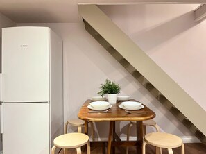 A compact kitchen with a white Bosch refrigerator, a wooden dining table with four stools, and a staircase. - Apartment for 8 guests in Jewish Disctrict Cracow, Bożego Ciała (Kraków)