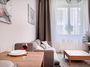 A living room with a sofa, a dining table, and a window with sheer curtains. - Premium Apartment for 3 guest with A/C in Cracow, Dąbrowskiego (Kraków)
