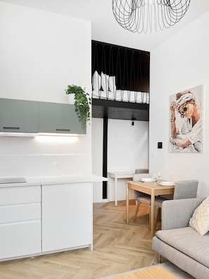 A modern kitchen with white cabinetry, a dining area with a wooden table, and a gray sofa. - Premium Apartment for 3 guest with A/C in Cracow, Dąbrowskiego (Kraków)