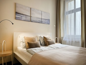 A neatly made bed with multiple pillows, a bedside table, and a wall-mounted artwork. - Beautiful Studio for 4 guests, Main Square, Cracow, Marka (Kraków)