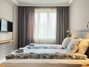 Ein Hotelzimmer mit Bett, einem flachbildfernseher an der Wand und einem fenster mit vorhängen.