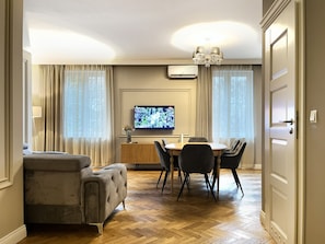 A modern living room with a sofa, dining table, chairs, a TV, and a chandelier. - 3-room Premium Apartment for 6 guests city center, Beliny Prażmowskiego (Kraków)