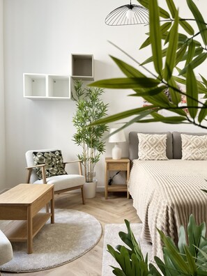 A modern bedroom with a bed, bedside tables, a chair, a small table, a potted plant, and a hanging light fixture. - Premium Apartament z AC, Cracow city center, Dąbrowskiego (Kraków)
