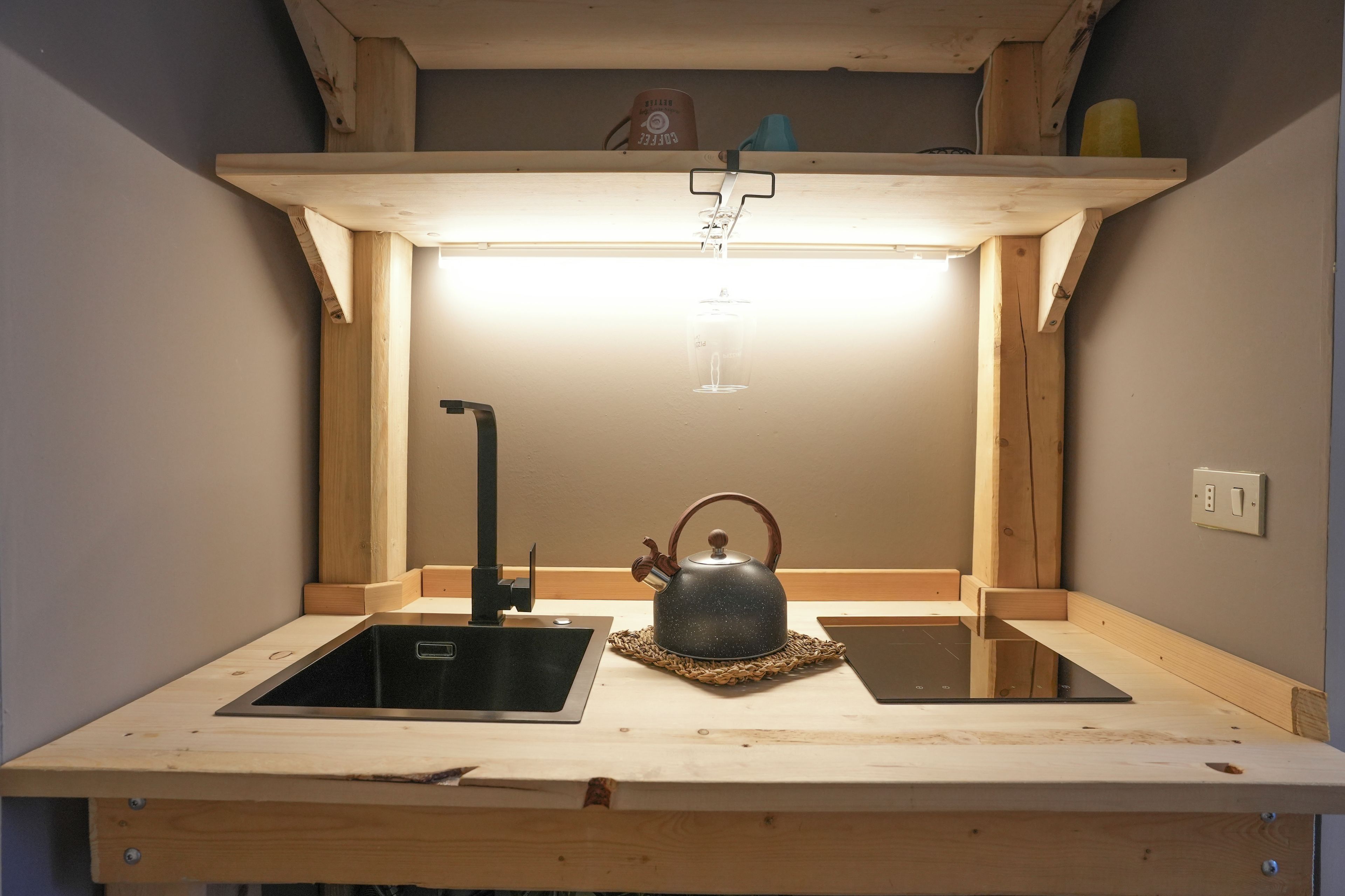 Una cucina compatta con un lavandino, un bollitore e un piccolo piano di lavoro.
