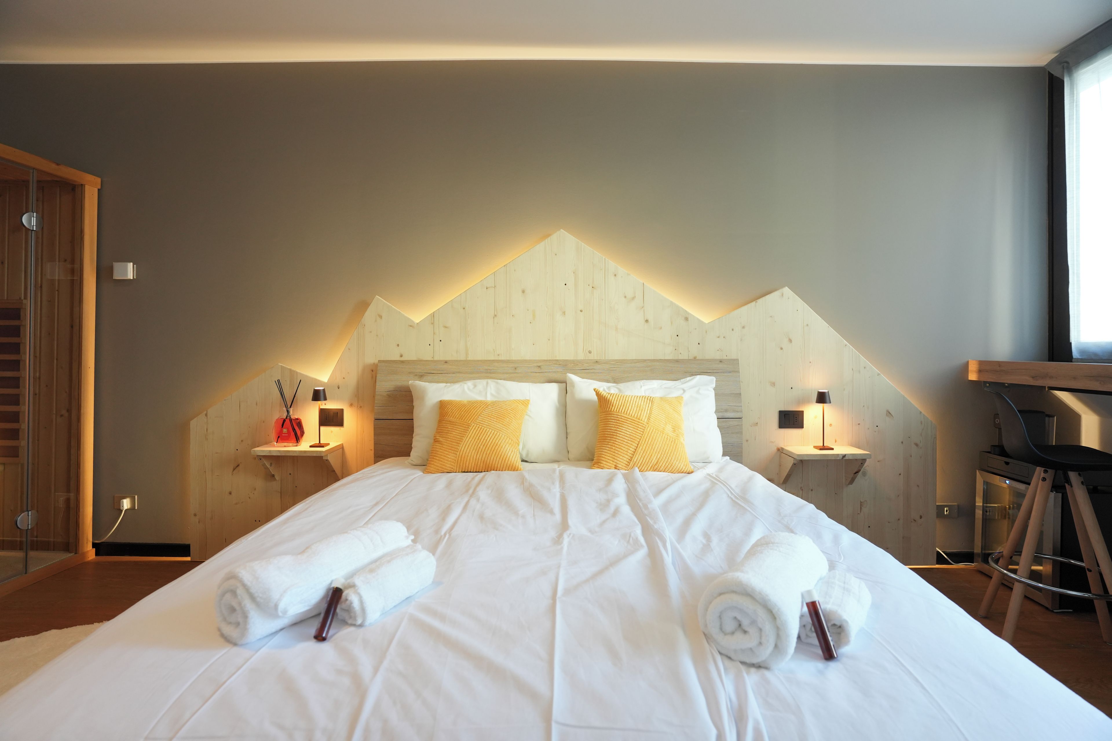 Une chambre d’hôtel avec un grand lit, deux tables de chevet avec des lampes, une tête de lit en bois et une fenêtre sur le côté droit.