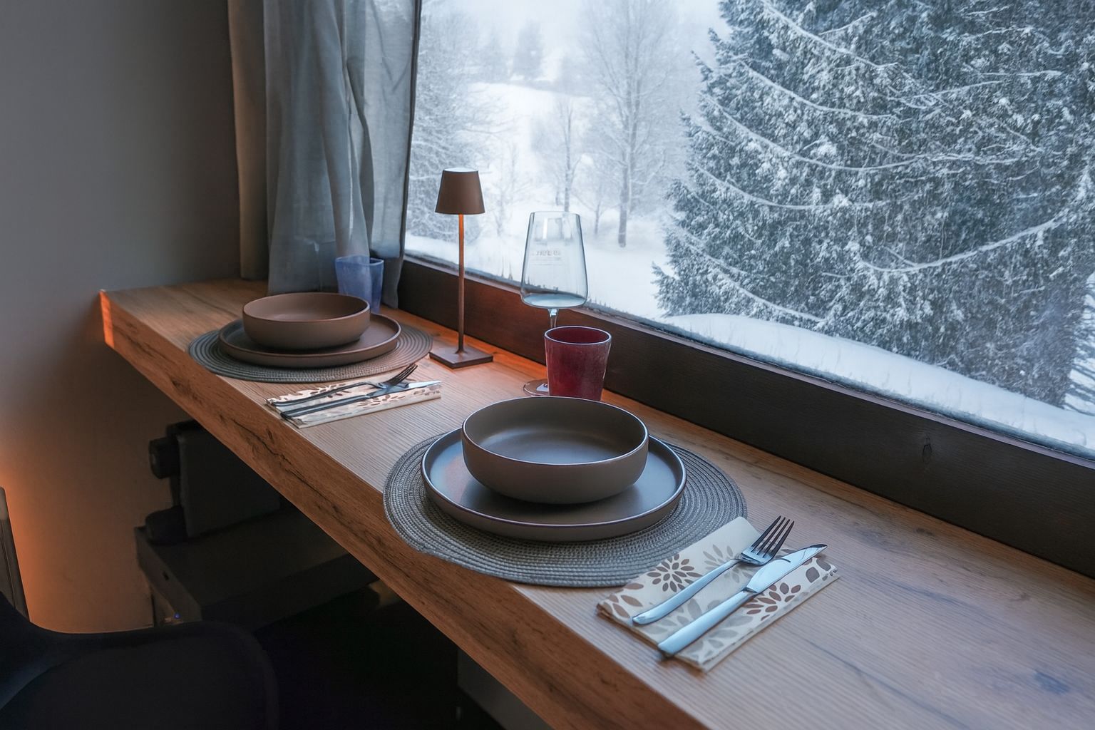 Un tavolo imbandito con piatti, posate e un bicchiere, vicino a una finestra con vista innevata.