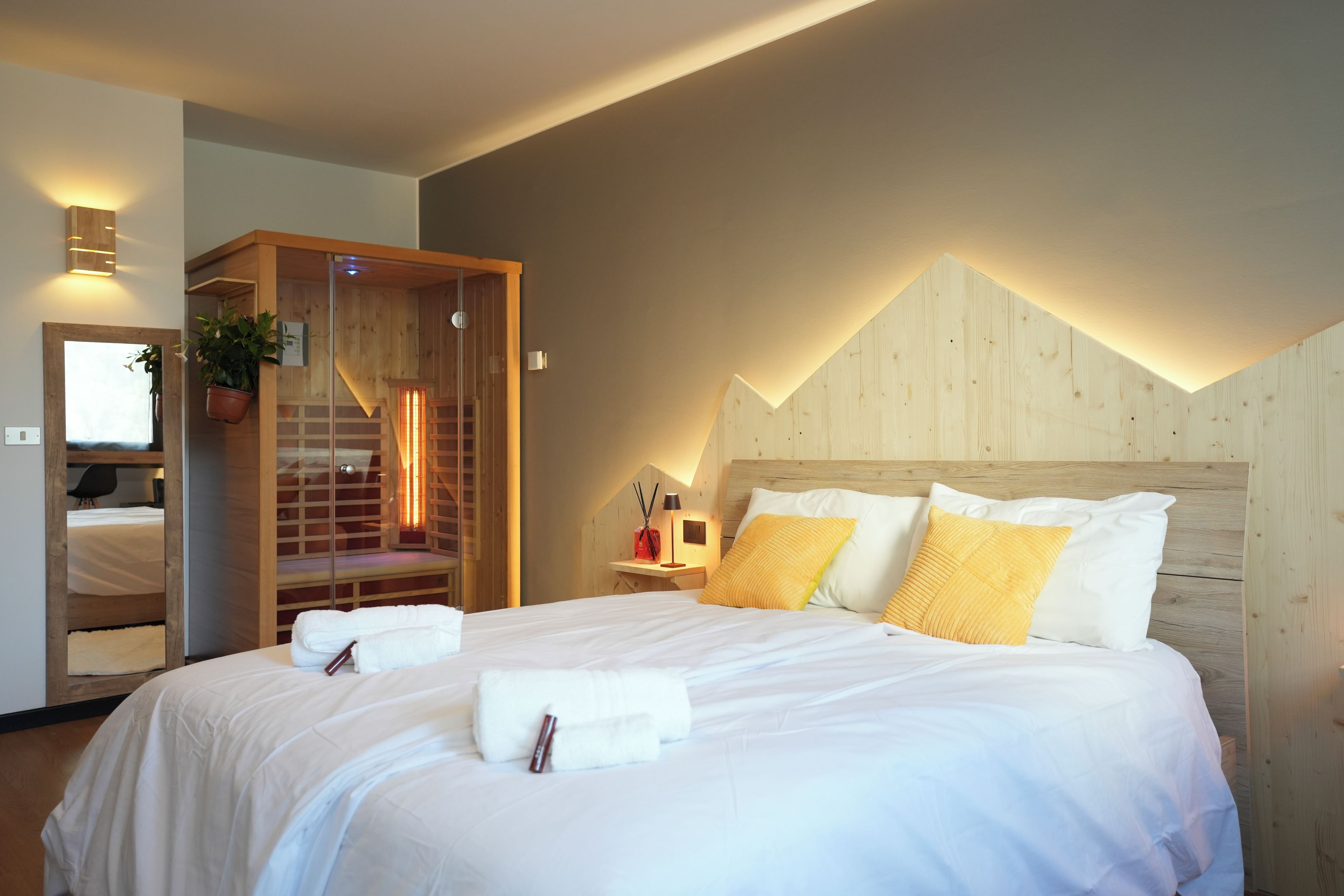A hotel room with a large bed, a wooden headboard, a built-in sauna, and a mirror.