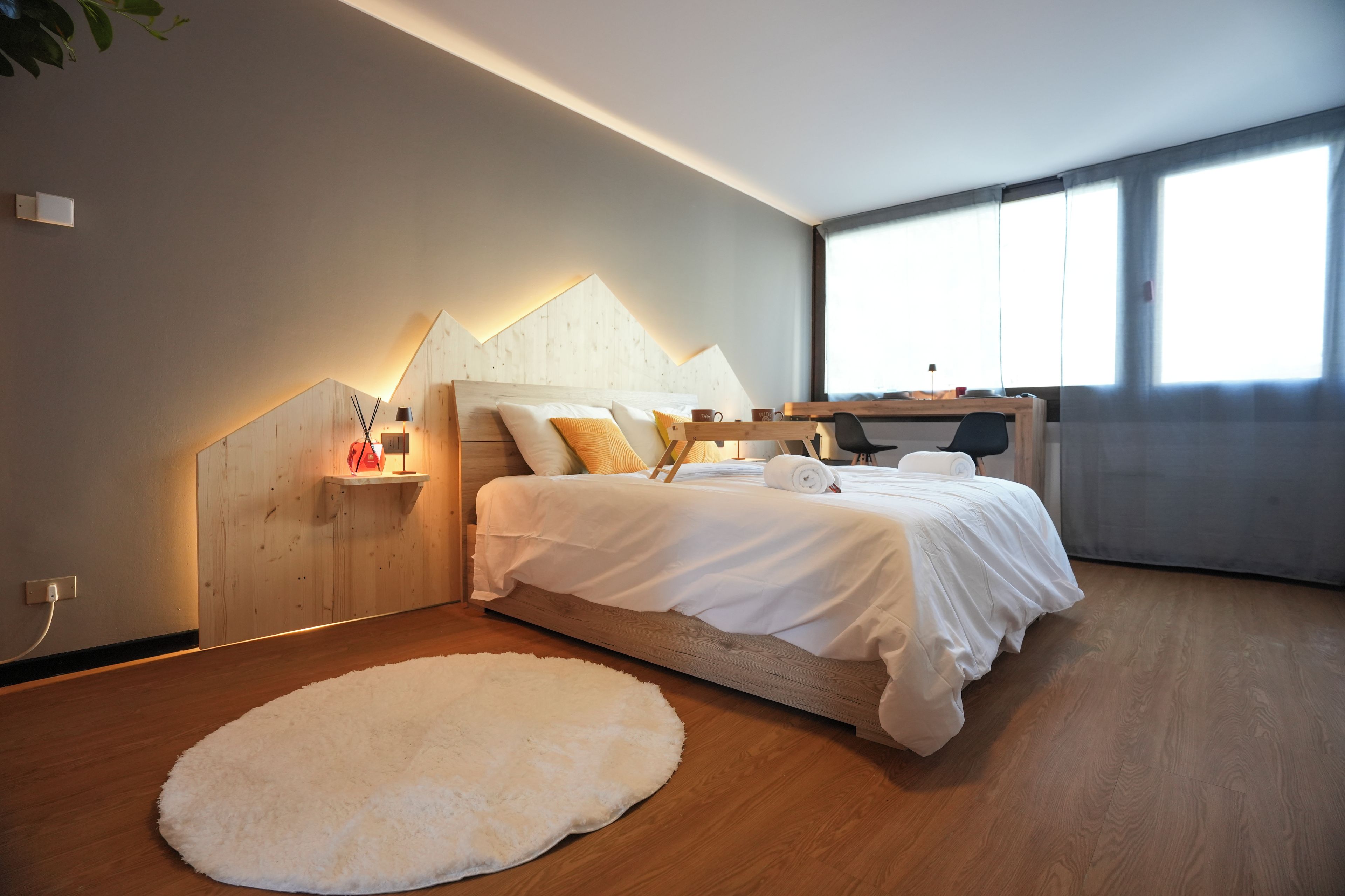 Une chambre moderne avec un lit en bois, un tapis blanc et un bureau avec une chaise.