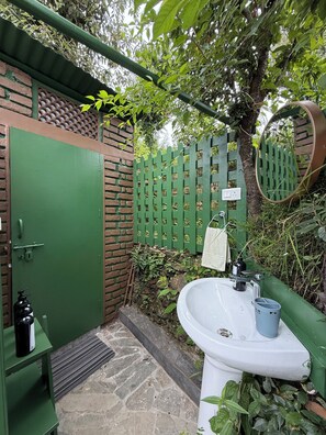 A small outdoor bathroom with a green door, a white sink, and a green fence with a mirror. - Shoonya (Mukteshwar)