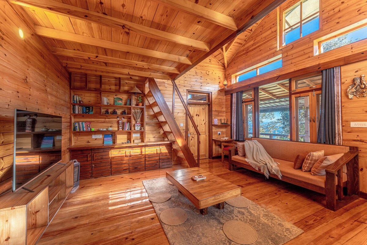A wooden cabin interior with a staircase, a sofa, a coffee table, and bookshelves.