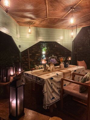 A cozy dining area with a stone archway, wooden ceiling, and tables set with tablecloths and centerpieces. - Shoonya (Mukteshwar)