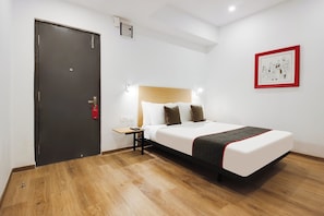 Ett hotellrum med en säng, ett sängbord, en väggmonterad lampa och en dörr.