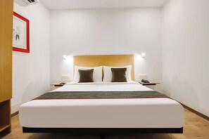 A hotel room with a bed, bedside tables, a wall-mounted light, and a framed picture.